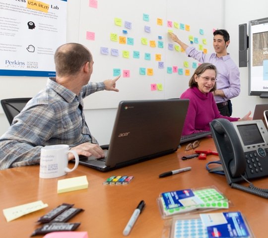 Employees working at a table and using sticky notes on the wall